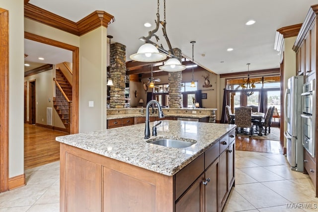 kitchen with light stone counters, pendant lighting, ornamental molding, a sink, and an island with sink