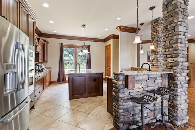 kitchen with a center island with sink, stainless steel refrigerator with ice dispenser, a sink, decorative light fixtures, and light stone countertops