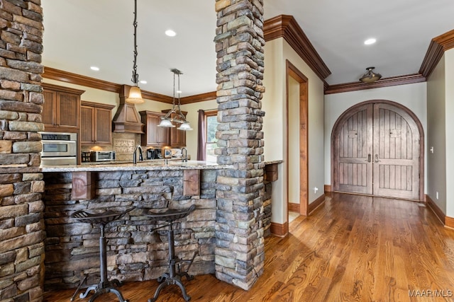 kitchen with dark wood-type flooring, oven, decorative light fixtures, custom exhaust hood, and a kitchen bar