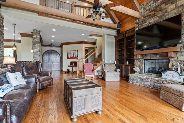 living room featuring built in shelves, ceiling fan, beamed ceiling, a stone fireplace, and wood finished floors