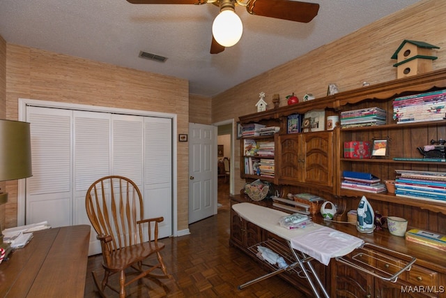 office area featuring dark parquet flooring, ceiling fan, wooden walls, and a textured ceiling