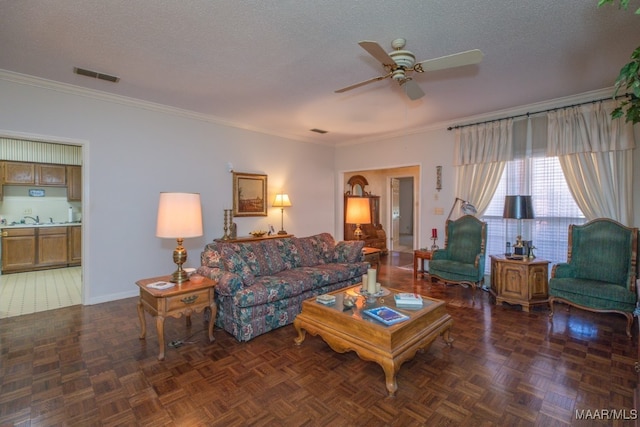 living area featuring a textured ceiling, a ceiling fan, visible vents, and crown molding