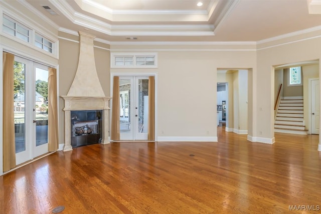 unfurnished living room featuring a tray ceiling, crown molding, french doors, and hardwood / wood-style floors