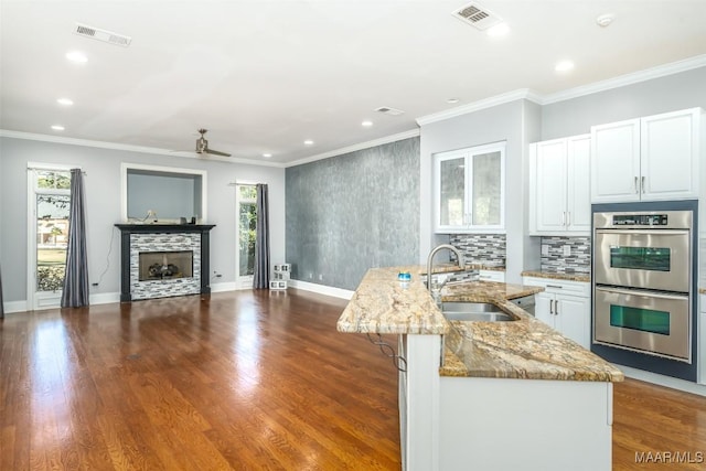 kitchen featuring stainless steel double oven, sink, a center island with sink, white cabinets, and plenty of natural light