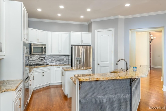 kitchen with a center island with sink, white cabinets, sink, appliances with stainless steel finishes, and wood-type flooring