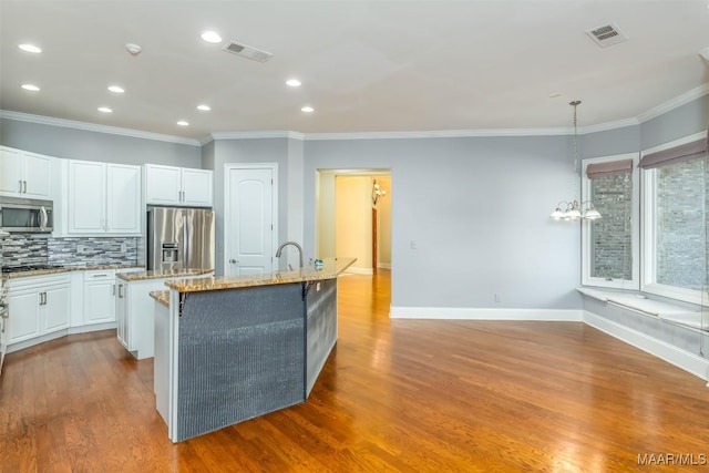 kitchen featuring decorative light fixtures, stainless steel appliances, a kitchen island with sink, and light hardwood / wood-style floors