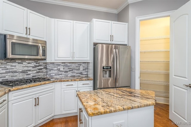 kitchen featuring appliances with stainless steel finishes, light stone counters, wood-type flooring, white cabinets, and a center island