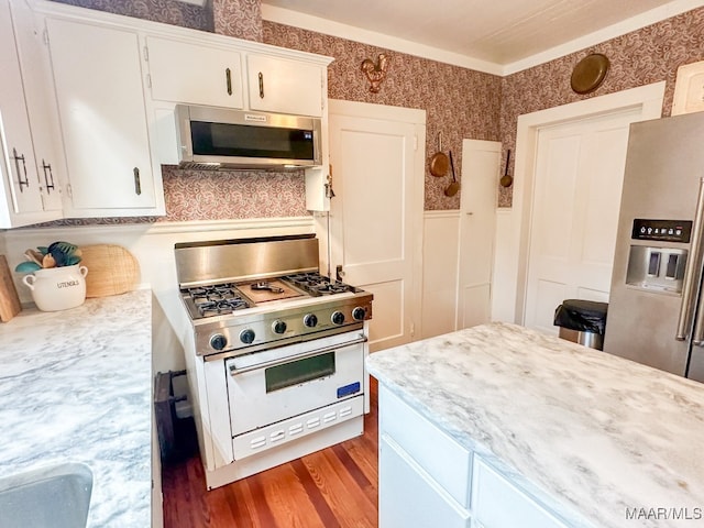 kitchen featuring appliances with stainless steel finishes, white cabinetry, wood-type flooring, and ornamental molding