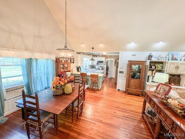 dining space with cooling unit, light hardwood / wood-style flooring, high vaulted ceiling, and a chandelier