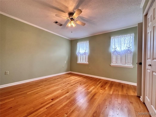 empty room featuring baseboards, visible vents, a ceiling fan, ornamental molding, and light wood-style floors