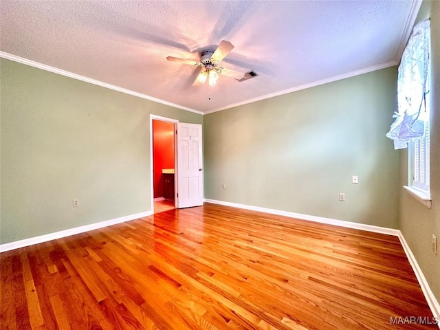 spare room with a textured ceiling, ornamental molding, light wood-type flooring, and baseboards