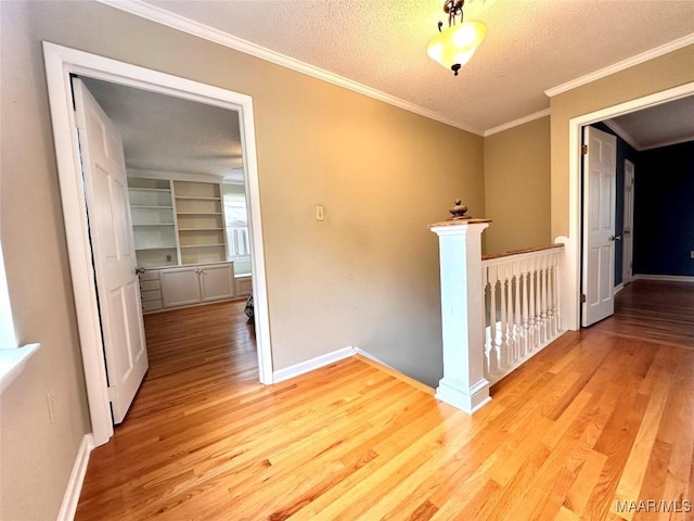 corridor with a textured ceiling, an upstairs landing, baseboards, light wood-type flooring, and crown molding