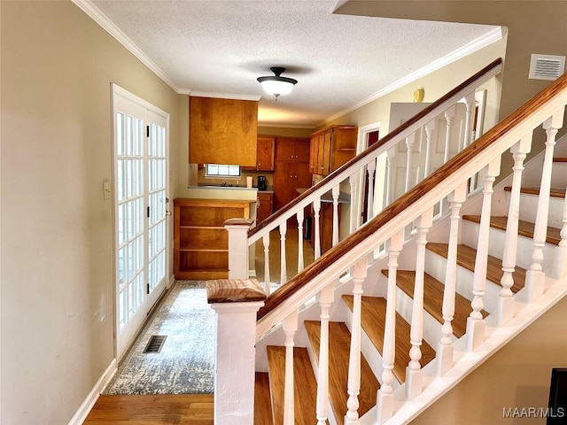 stairway with ornamental molding, visible vents, a textured ceiling, and wood finished floors