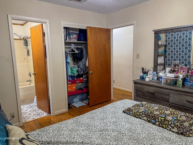 bedroom with a textured ceiling, connected bathroom, hardwood / wood-style floors, and a closet