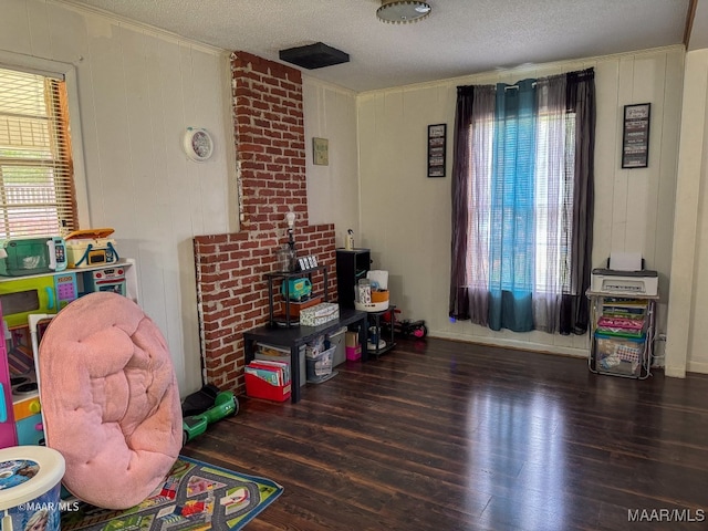 game room with wood walls, a wealth of natural light, dark hardwood / wood-style flooring, and a textured ceiling