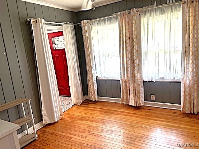 spare room with crown molding, wood walls, and light wood-type flooring