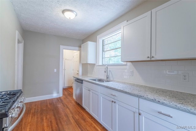 kitchen with backsplash, appliances with stainless steel finishes, wood-type flooring, sink, and white cabinetry