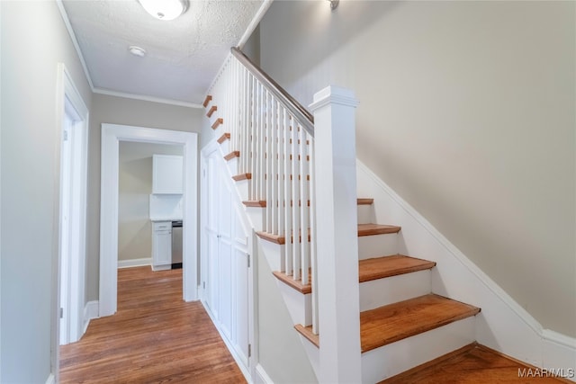 stairway with hardwood / wood-style floors, ornamental molding, and a textured ceiling