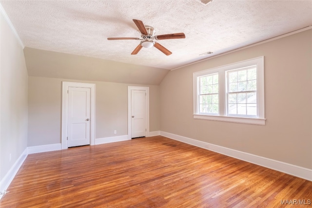 spare room with a textured ceiling, ceiling fan, light wood-type flooring, and vaulted ceiling