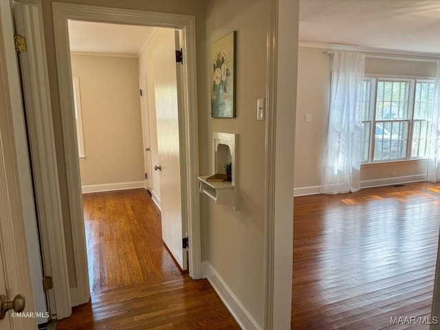 hallway featuring dark wood-style floors, baseboards, and ornamental molding