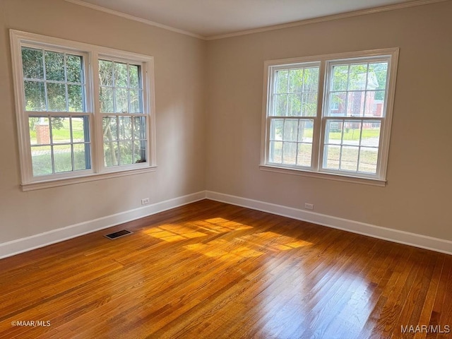 unfurnished room with visible vents, hardwood / wood-style floors, baseboards, and ornamental molding