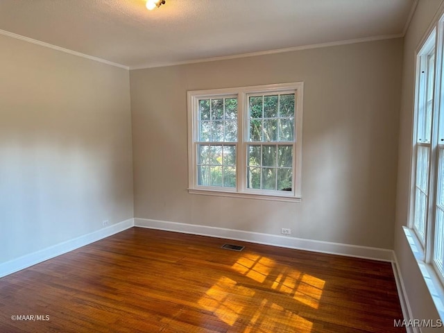 empty room featuring visible vents, baseboards, dark wood-style flooring, and crown molding