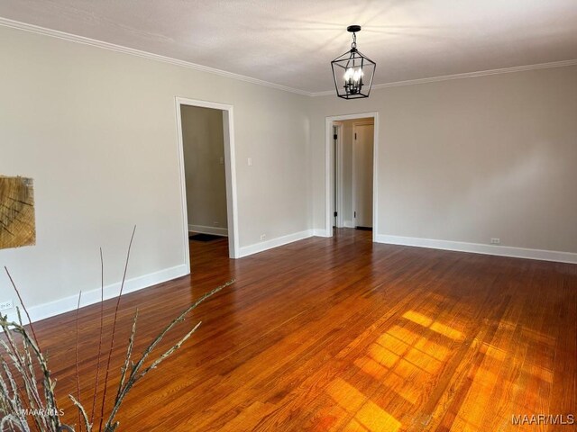 spare room with baseboards, an inviting chandelier, wood finished floors, and crown molding