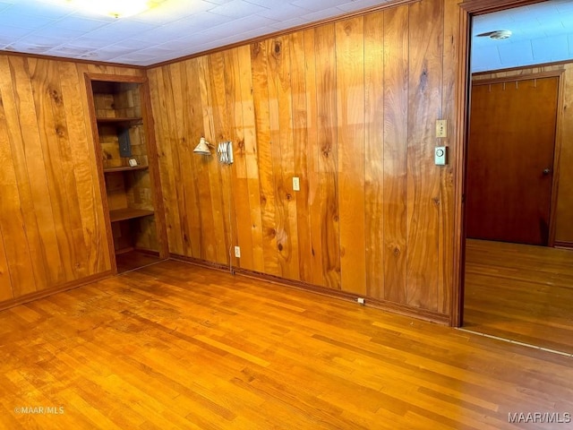 empty room featuring wooden walls, built in shelves, wood finished floors, and baseboards