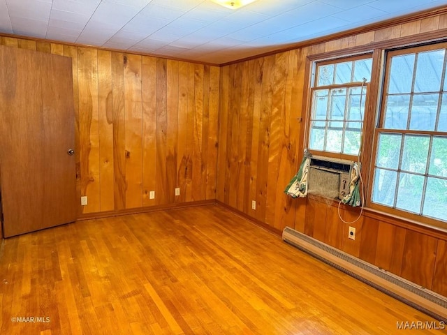 unfurnished room with wooden walls, wood finished floors, baseboards, and a baseboard radiator