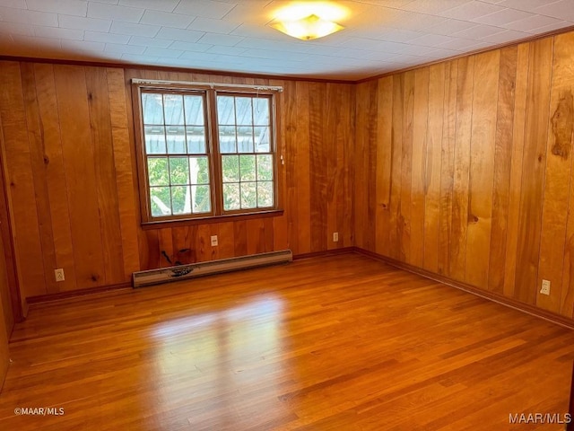 empty room with baseboard heating, wood walls, baseboards, and wood finished floors