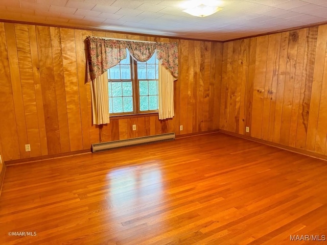 empty room featuring wooden walls, wood finished floors, baseboards, and baseboard heating