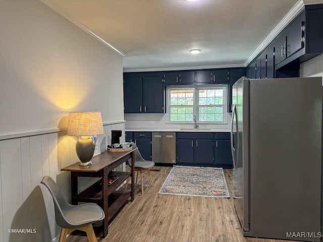 kitchen with a sink, stainless steel appliances, a wainscoted wall, and crown molding