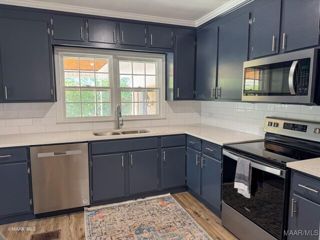 kitchen featuring blue cabinets, sink, light wood-type flooring, ornamental molding, and appliances with stainless steel finishes