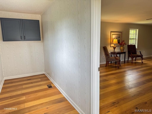 hall with light wood-type flooring, visible vents, baseboards, and ornamental molding