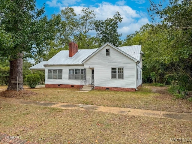 view of front of house featuring a front lawn, entry steps, metal roof, crawl space, and a chimney