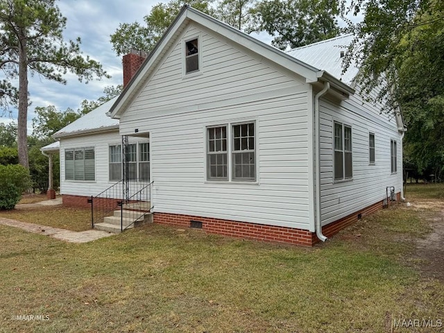 exterior space with a chimney, entry steps, crawl space, a lawn, and metal roof