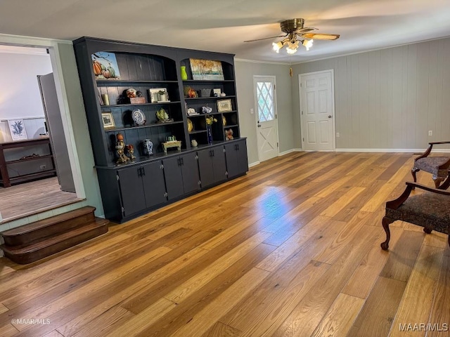 living area with crown molding, light wood-style floors, baseboards, and ceiling fan