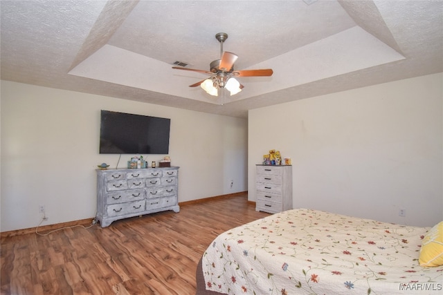 bedroom featuring a textured ceiling, ceiling fan, hardwood / wood-style floors, and a tray ceiling