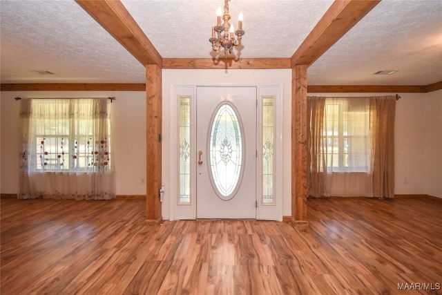 entrance foyer featuring light wood-type flooring, an inviting chandelier, a textured ceiling, and beam ceiling