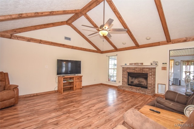 living room with ceiling fan, plenty of natural light, lofted ceiling with beams, and a brick fireplace