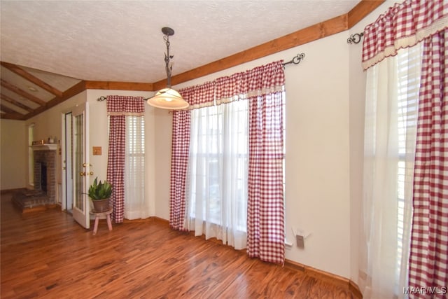 unfurnished dining area with a textured ceiling, plenty of natural light, wood-type flooring, and a brick fireplace