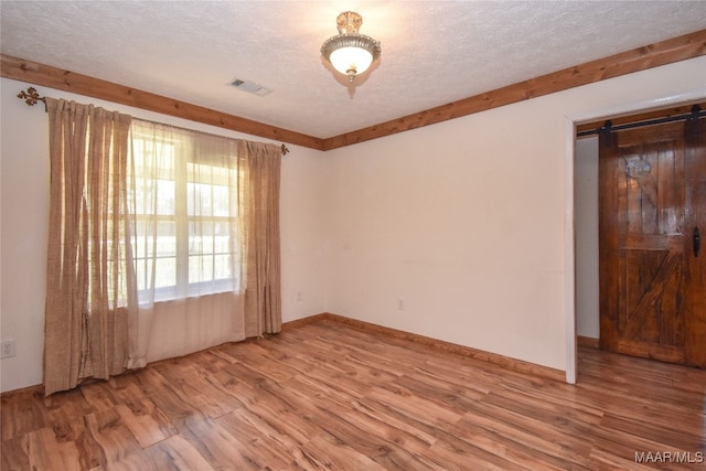 spare room featuring a textured ceiling, hardwood / wood-style flooring, and a barn door