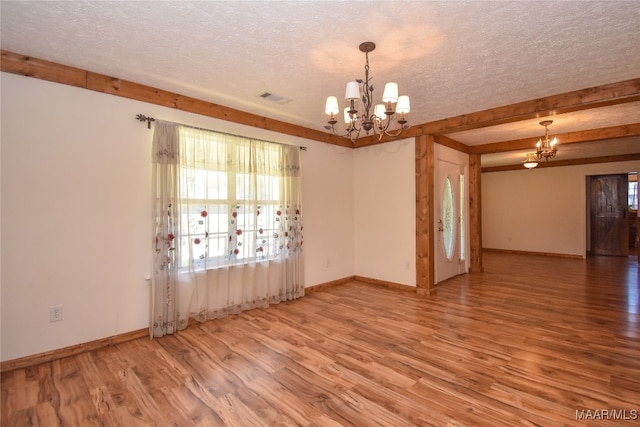 unfurnished room with a textured ceiling, a chandelier, hardwood / wood-style floors, and beamed ceiling