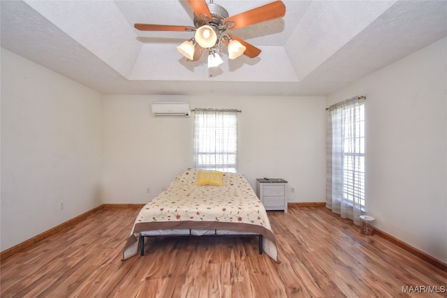 bedroom with multiple windows, a wall unit AC, and light hardwood / wood-style floors