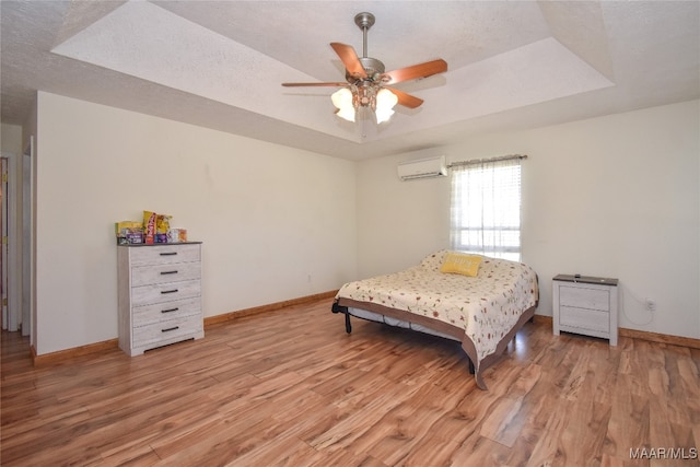 bedroom with a textured ceiling, a raised ceiling, ceiling fan, and light hardwood / wood-style flooring