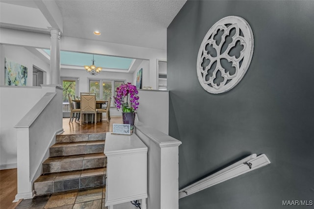 staircase featuring a notable chandelier, decorative columns, a textured ceiling, and hardwood / wood-style floors