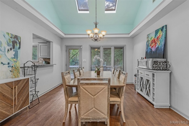 dining space with wood-type flooring, a notable chandelier, and lofted ceiling with skylight