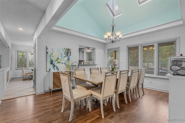 dining space with an inviting chandelier, vaulted ceiling with skylight, a textured ceiling, and hardwood / wood-style flooring