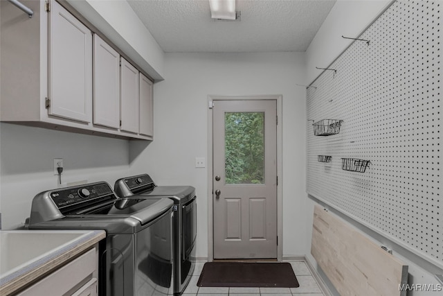 laundry room featuring light tile patterned floors, a textured ceiling, cabinets, sink, and washer and dryer