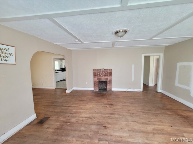 unfurnished living room with a textured ceiling, hardwood / wood-style flooring, and a brick fireplace